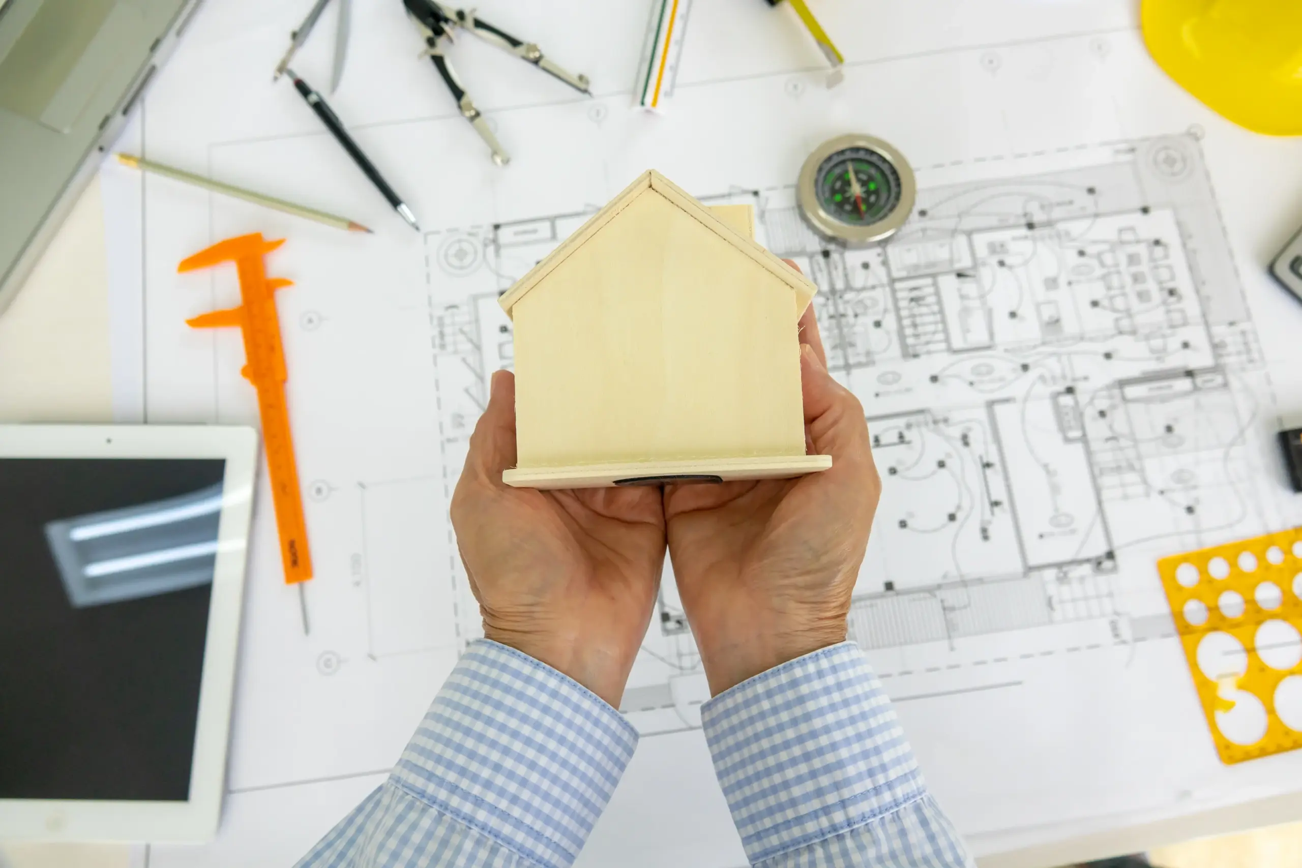 cropped-hand-architect-holding-model-home-blueprint-desk